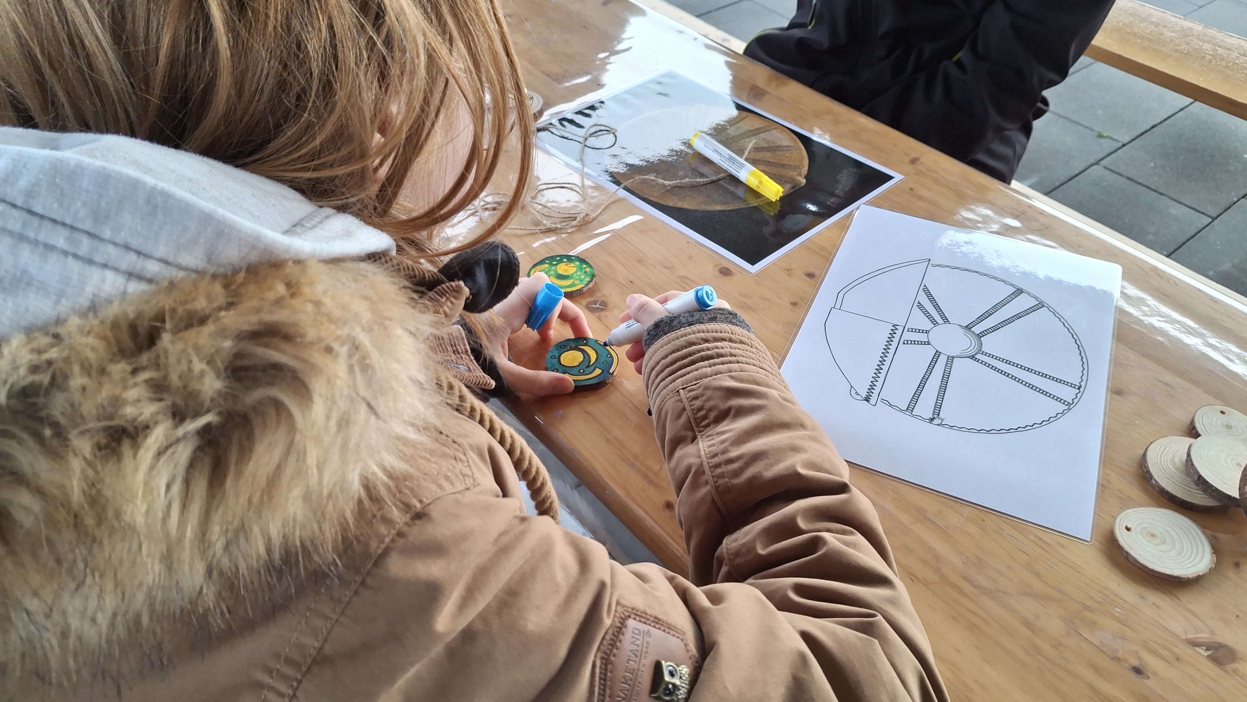 Ein Mädchen bemalt ein Holzamulette nach dem Vorbild der Himmelsscheibe von Nebra. 