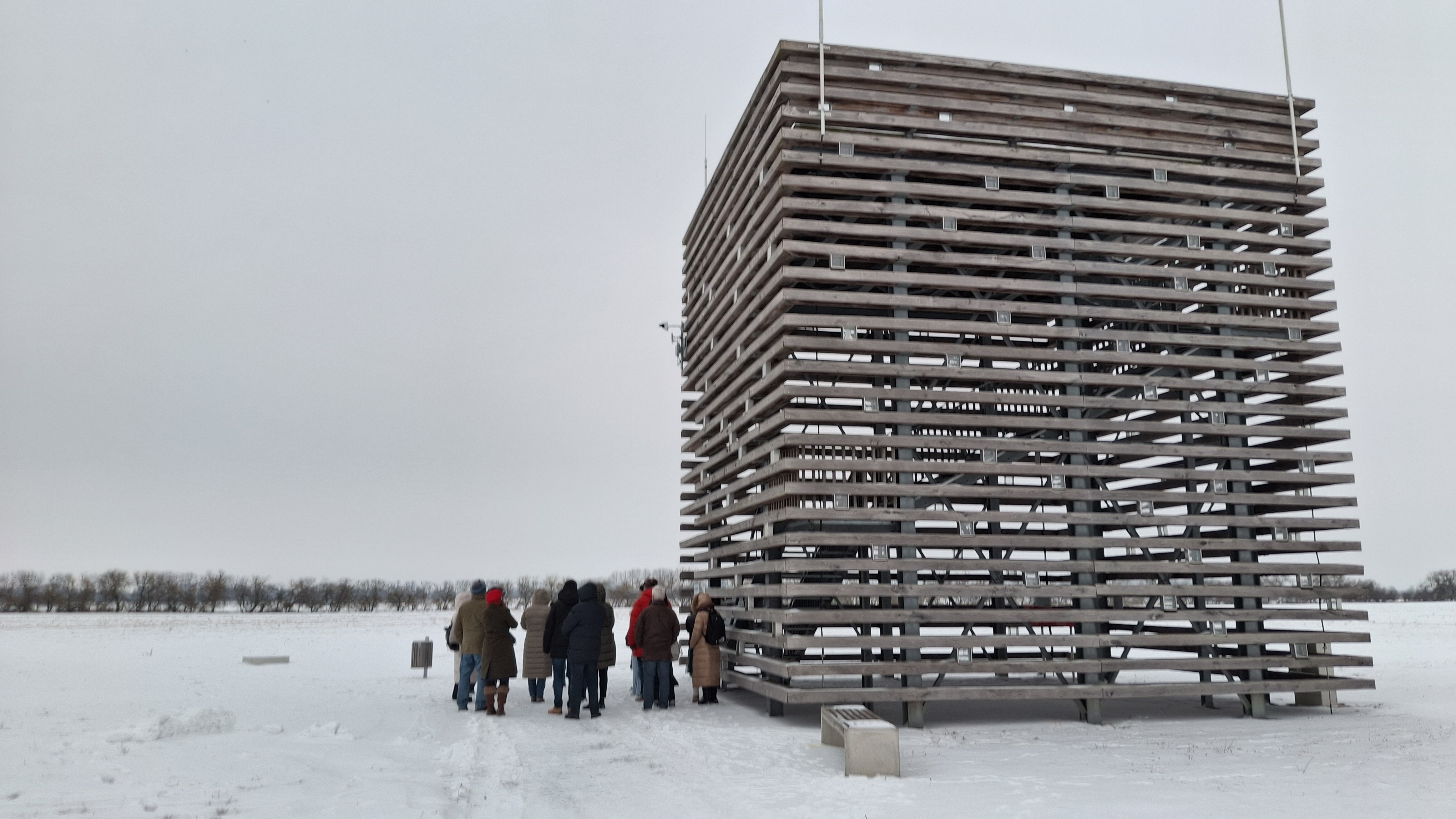 Neben dem Aussichtsturm auf dem Gelände des Ringheiligtums befindet sich eine Gruppe Personen, die an einer Gästeführung im Schnee teilnimmt.