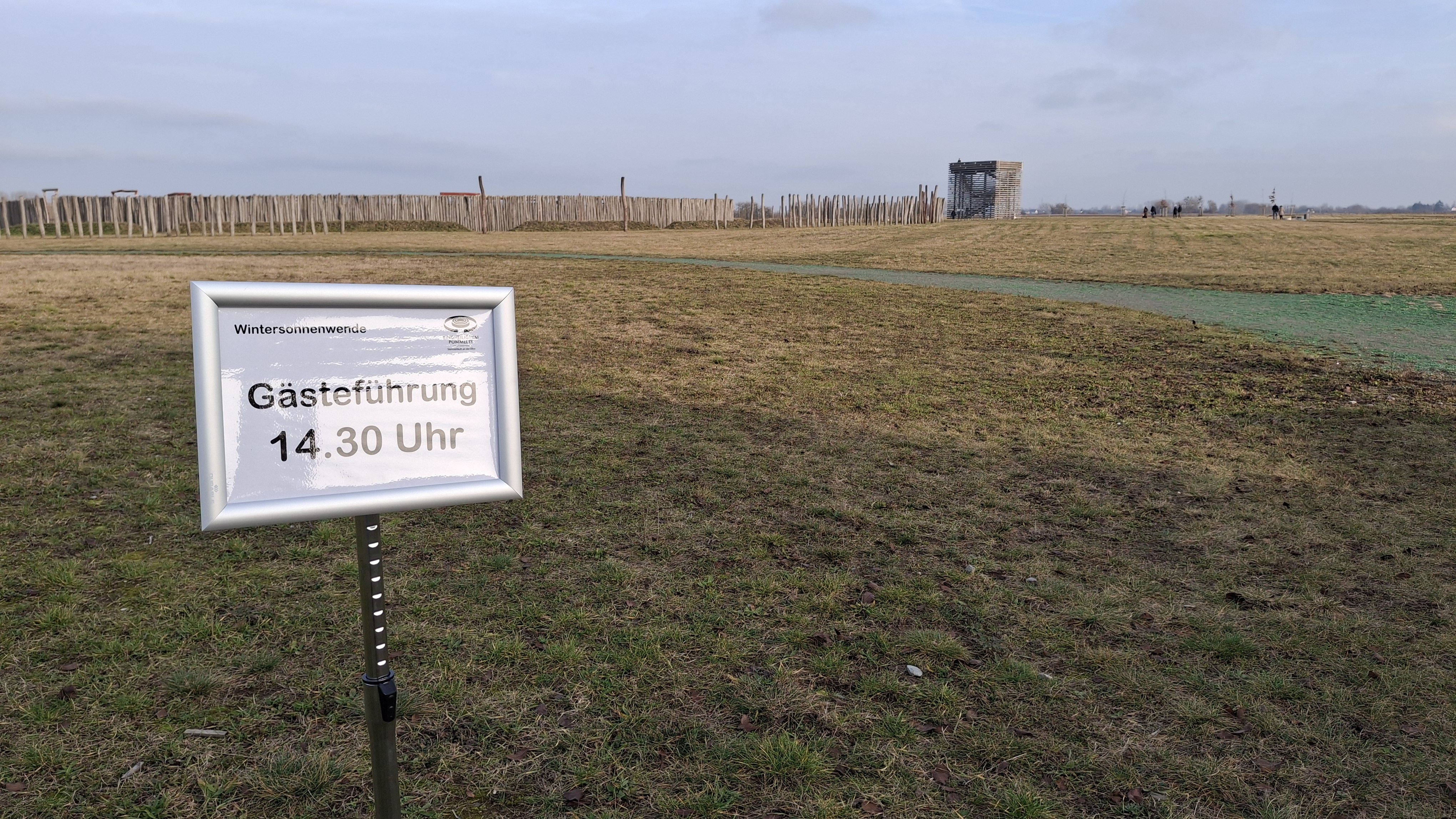 Auf dem Foto ist ein Schild für eine Gästeführung um 14:30 Uhr vor dem Hintergrund des Ringheiligtums zu sehen. 